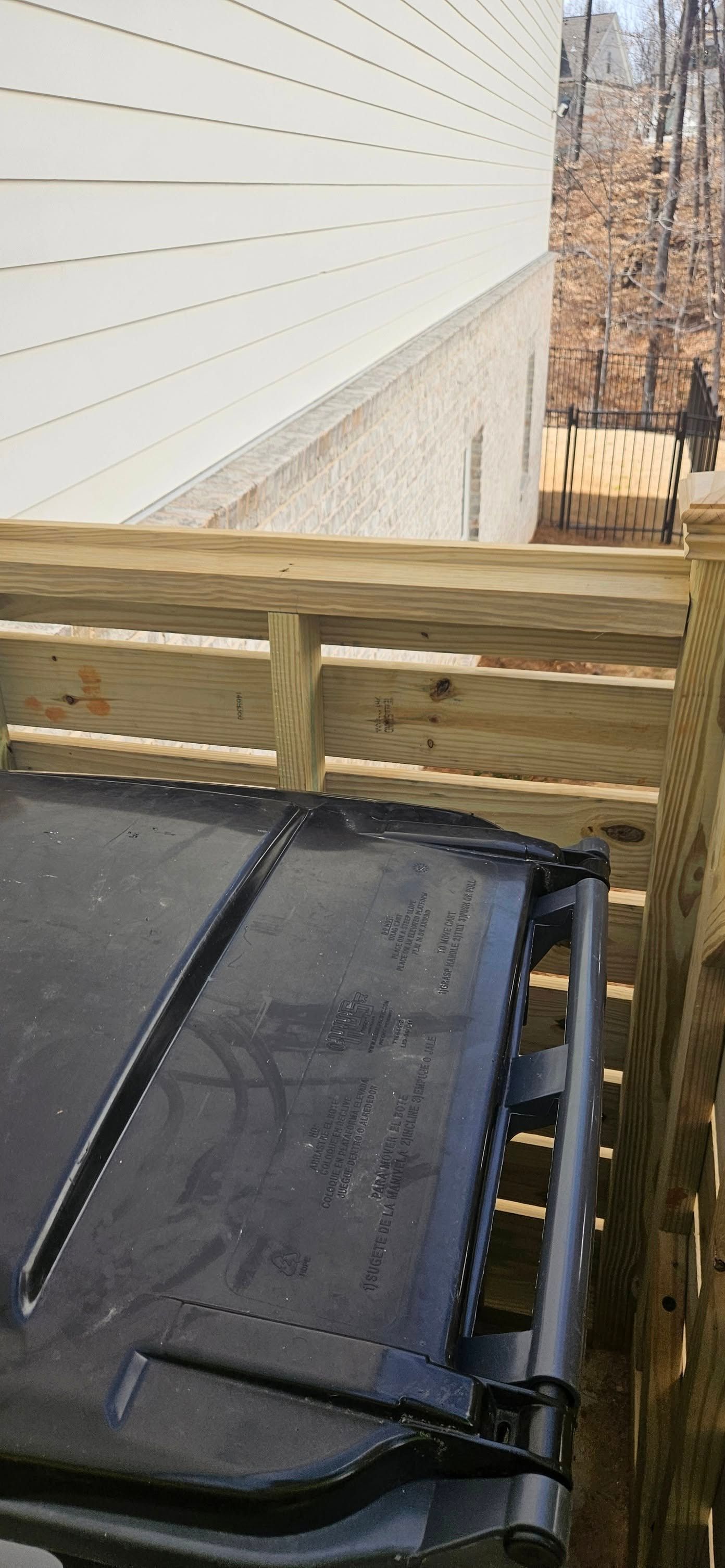 A dark, rectangular object is on wooden steps, with a wooden railing and a light-colored building in the background.