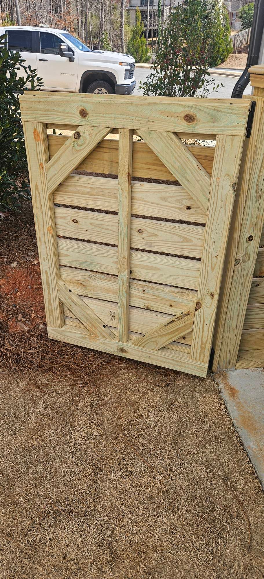 Wooden fence with diagonal supports, a vehicle, and greenery in the background.