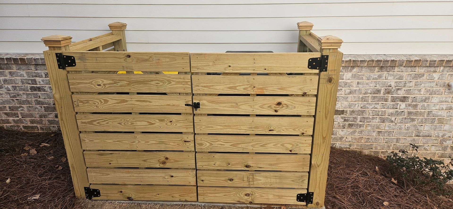 Wooden enclosure with doors, built against a brick and siding wall.