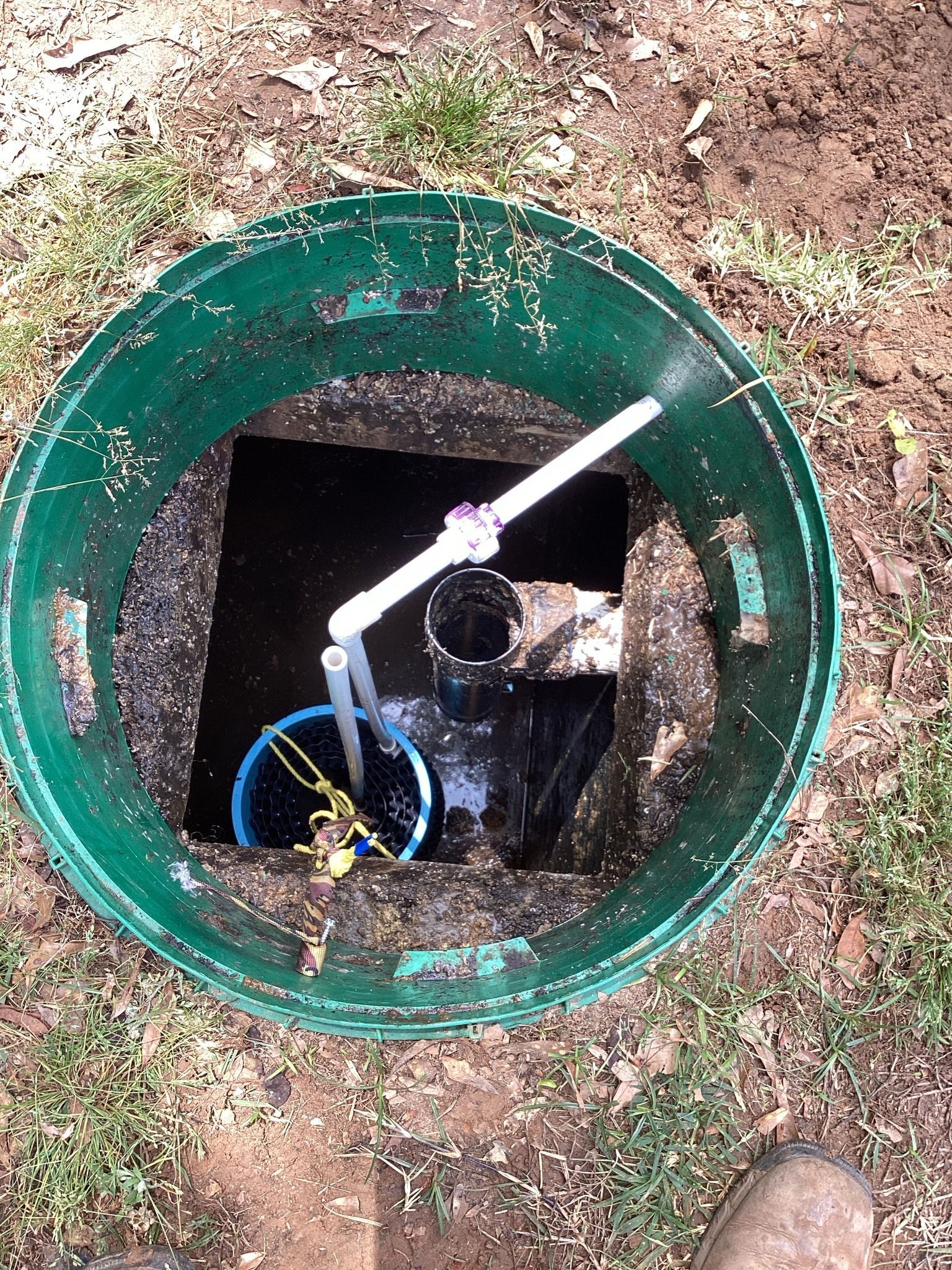 Green septic tank with pipes and pump inside, located in a grassy outdoor setting.