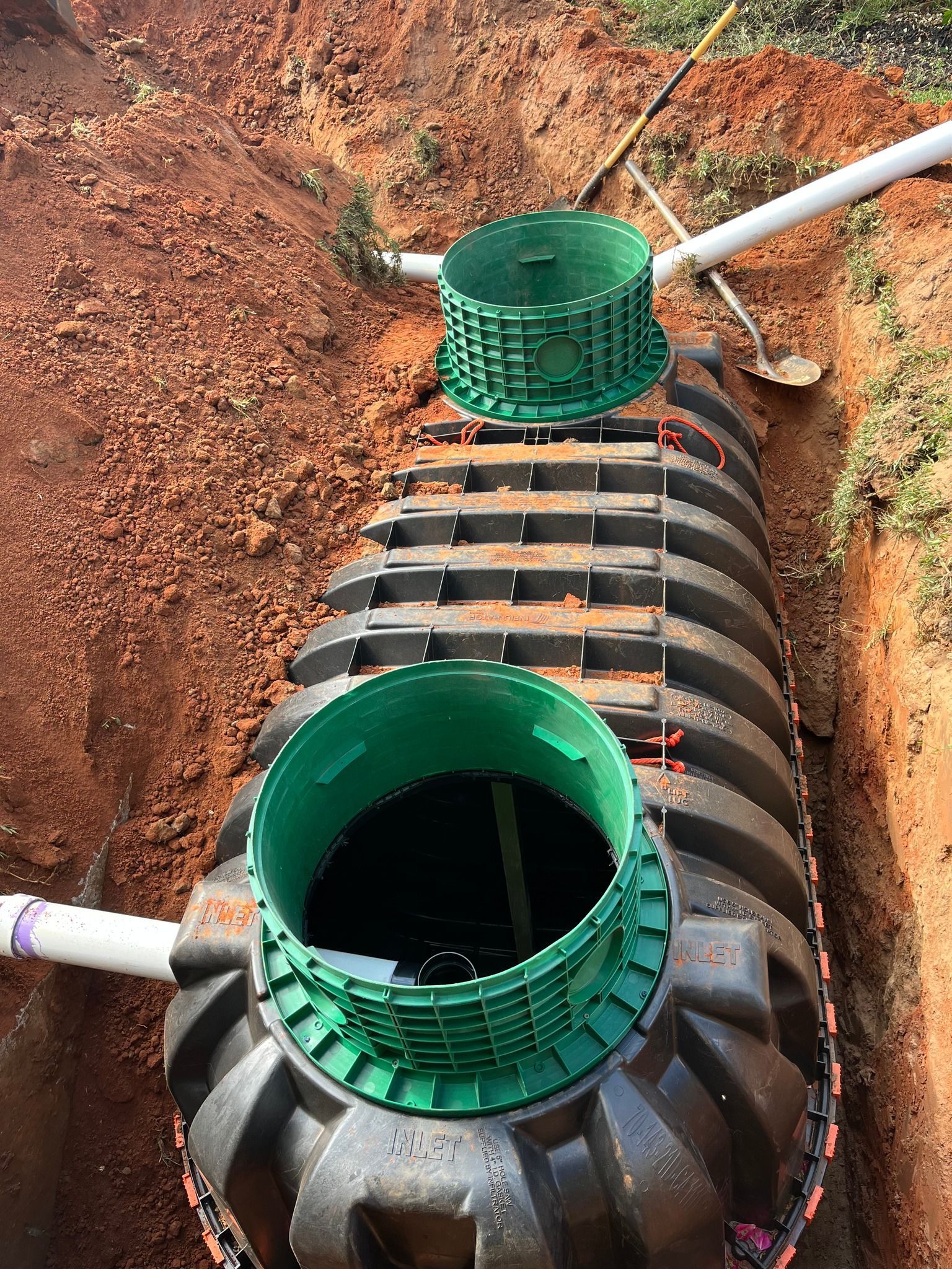 Septic tank installation in an open trench. Green access ports on dark tank in brown soil.