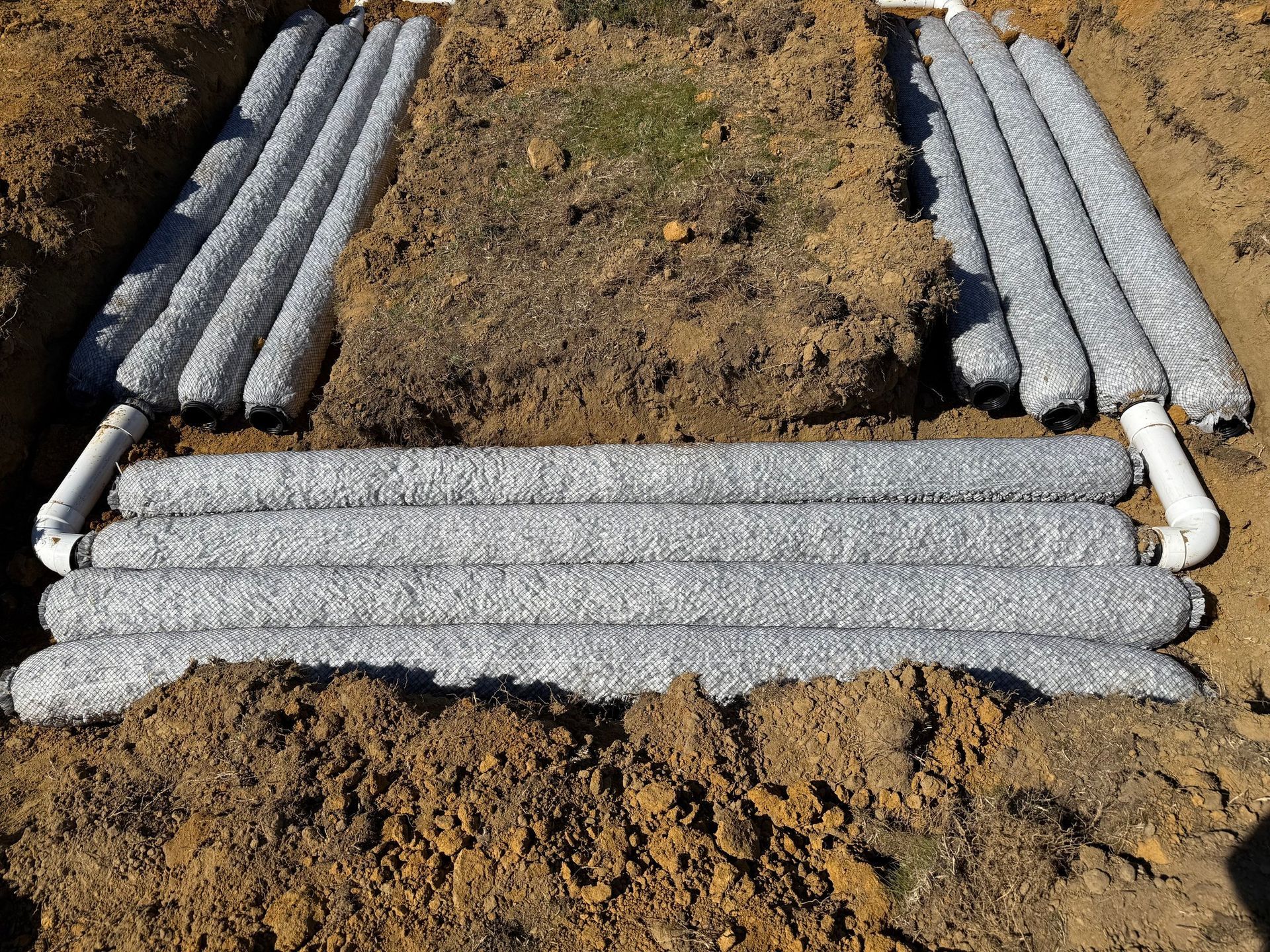 Underground gray gravel-filled drainage system installed in a trench with white PVC pipes.