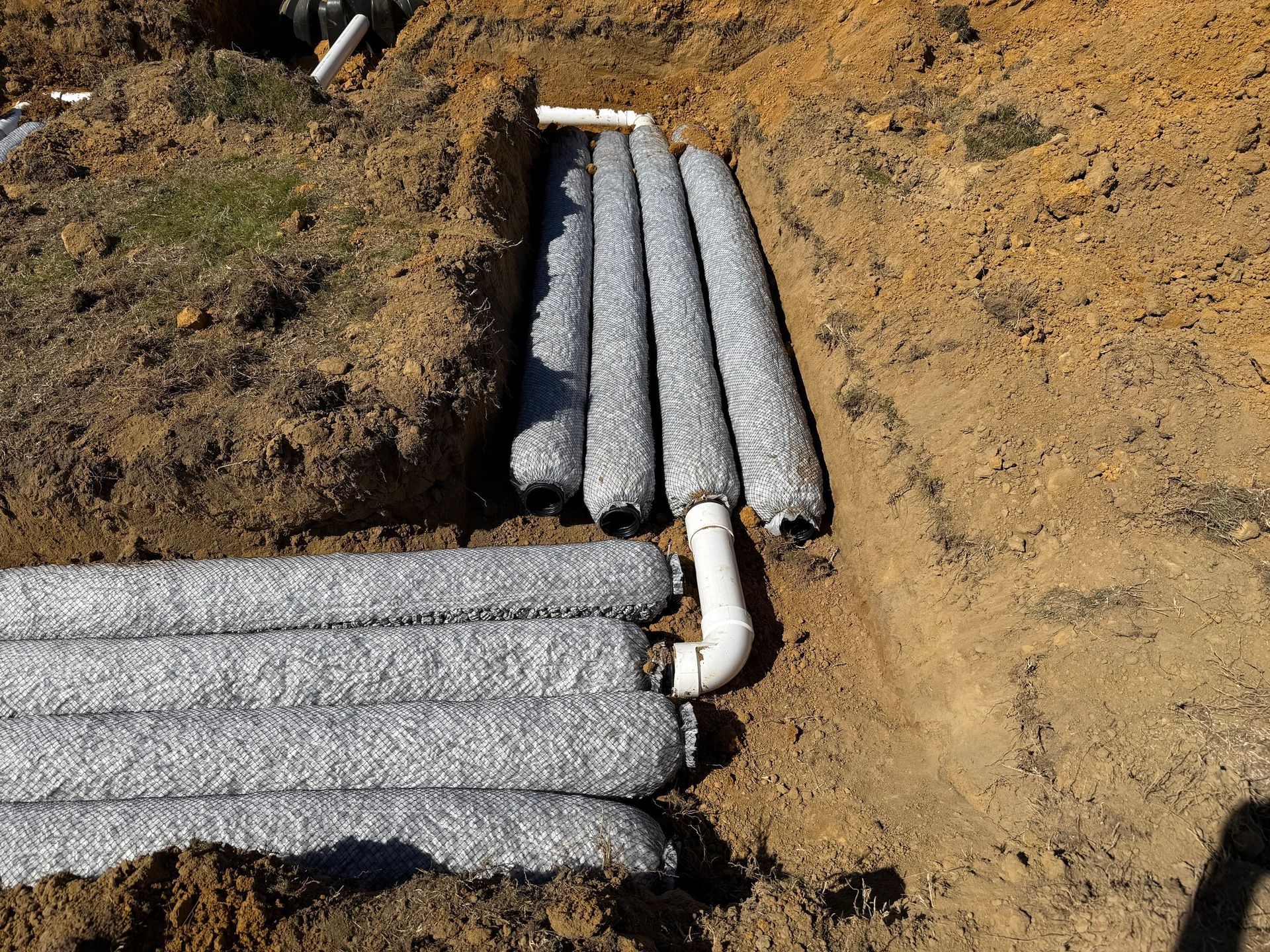 Installation of a gravel-filled drainage system with a white pipe in an excavated trench.