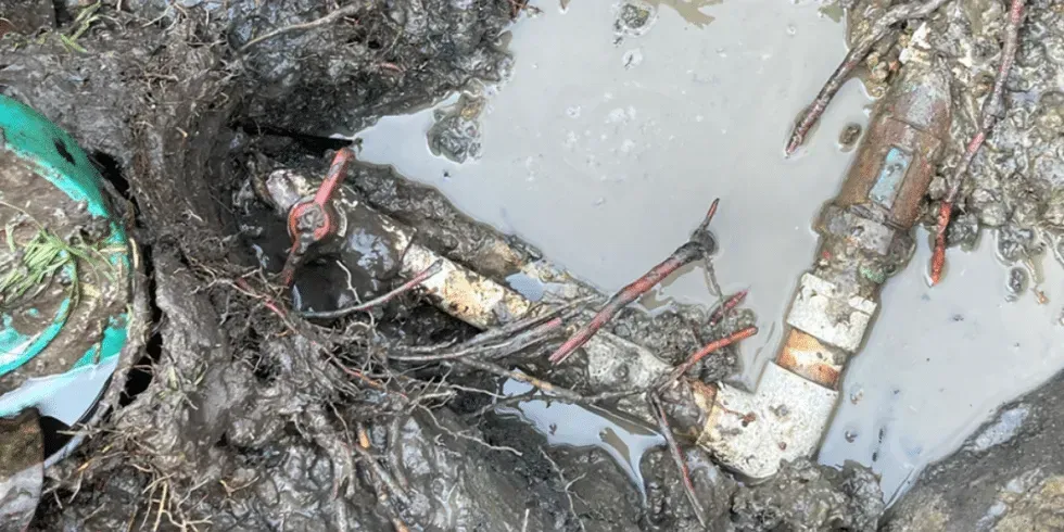 Muddy excavation with PVC pipes and a valve.