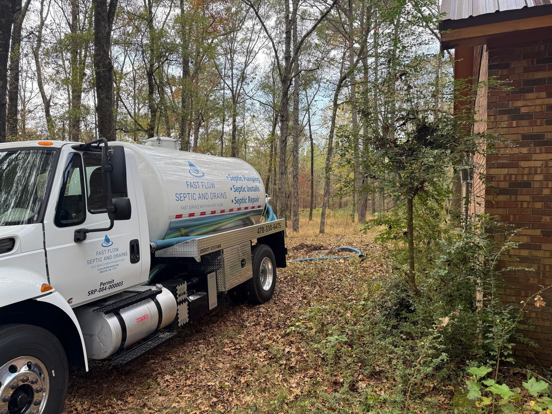 A yellow excavator digs a trench near a house, likely for construction or repair.