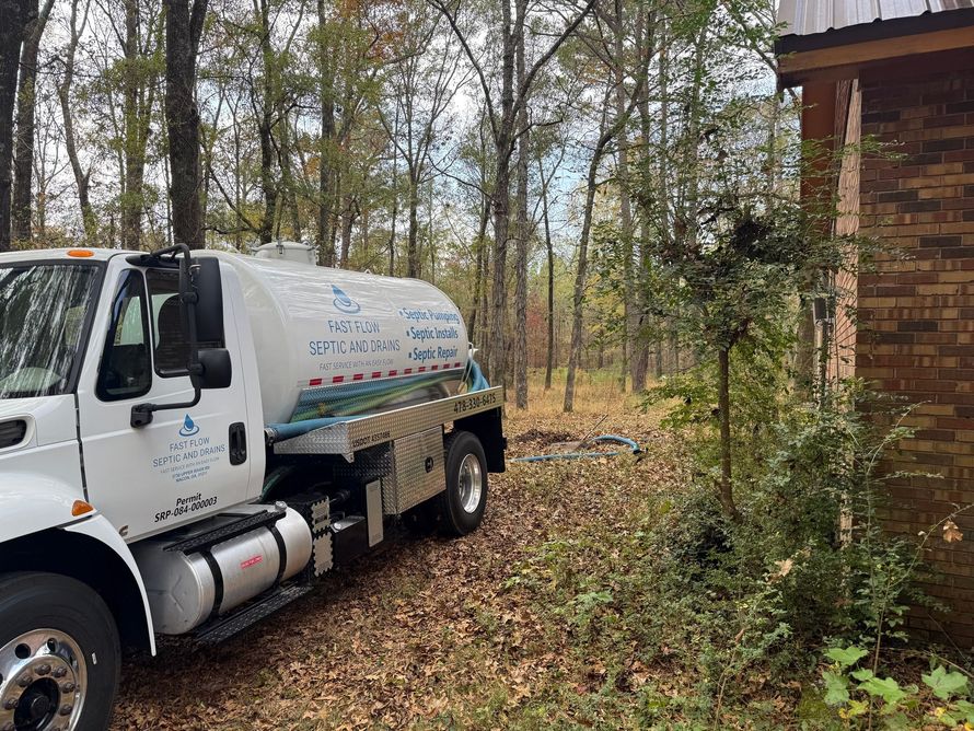 Black septic tank in a dirt hole, two access lids visible. Earth surrounds the tank.