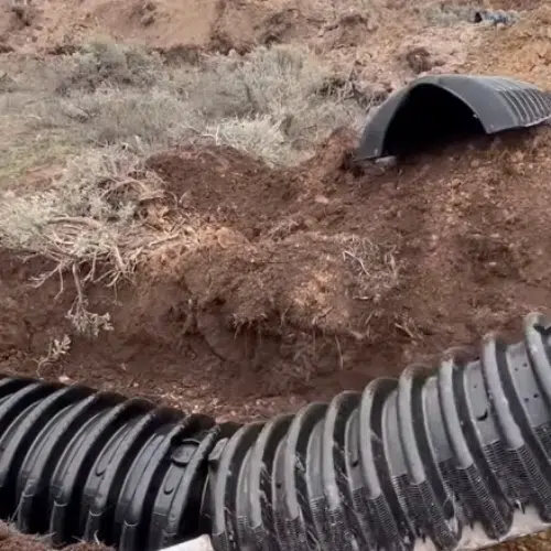 Black corrugated pipe in a dirt trench, connected to a partially buried culvert.