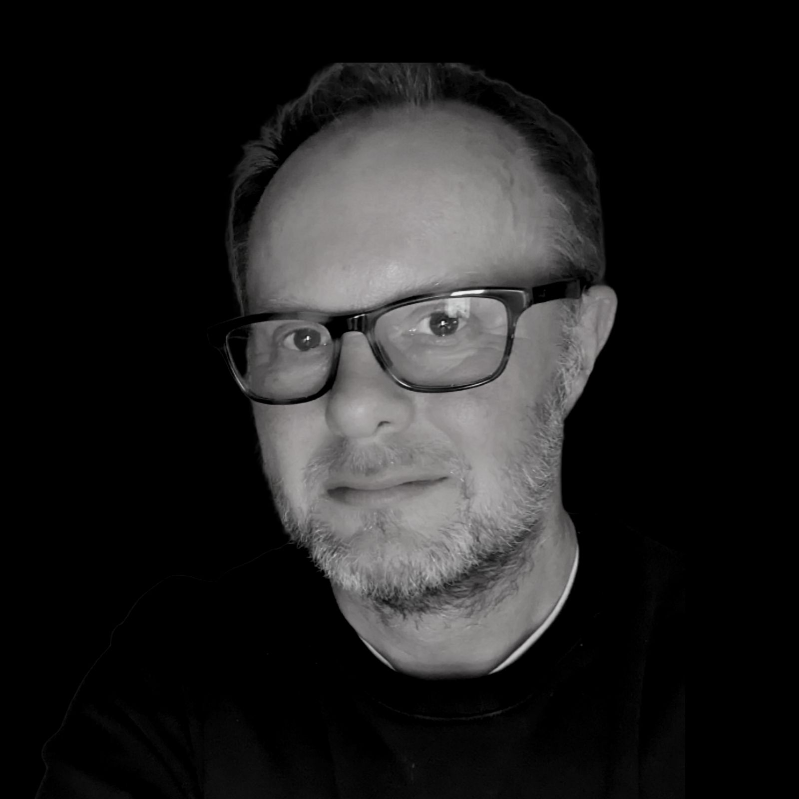a man with glasses and a beard is taking a selfie in a black and white photo .