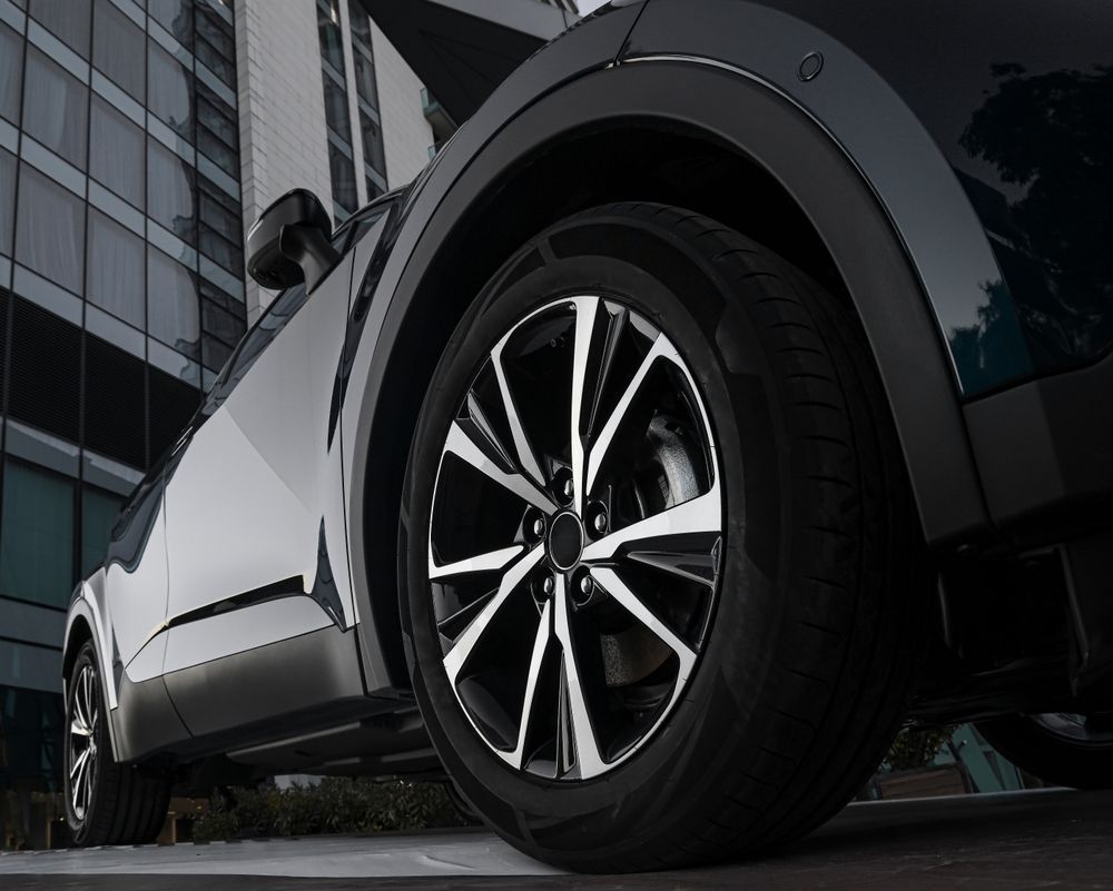 A close up of a car wheel with a building in the background.