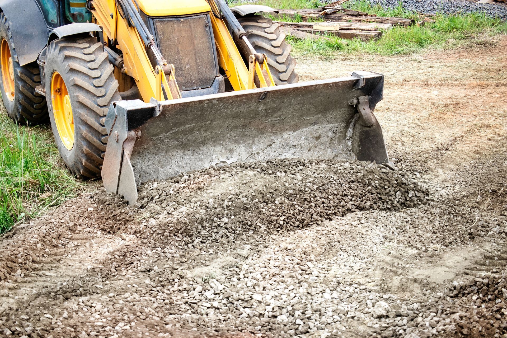 Yellow and black construction vehicle grading gravel on a dirt road.