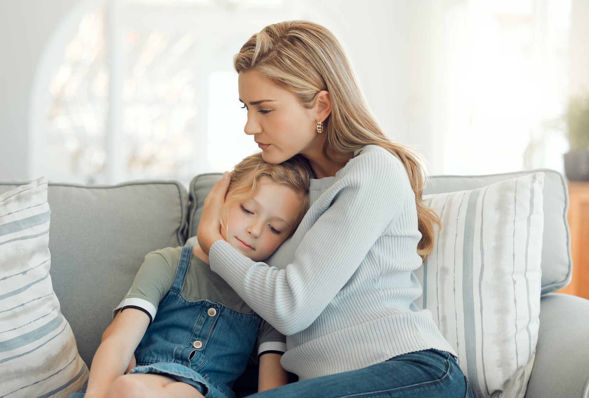 Woman comforting a child on a couch; woman's arm around the child's head, looking concerned.