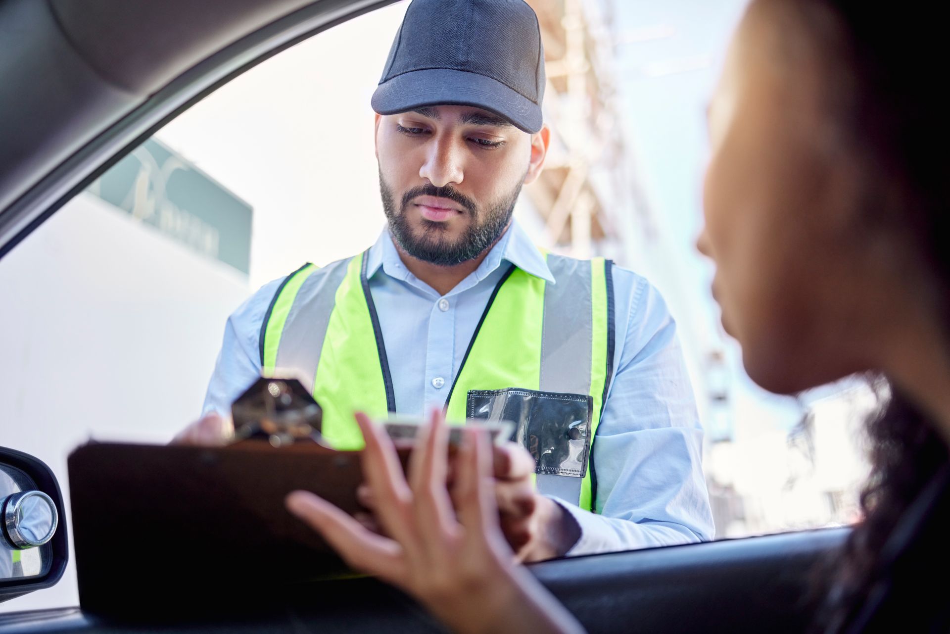 Security guard reviewing paperwork with a driver at a checkpoint.
