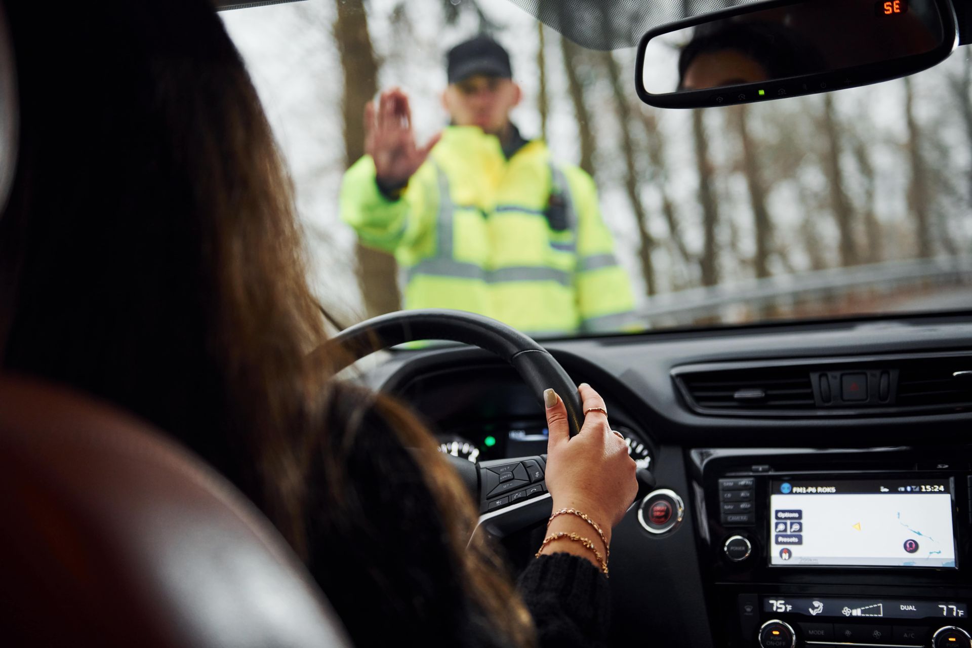 Woman driving car stopped by traffic officer in high-vis jacket, outdoor setting.