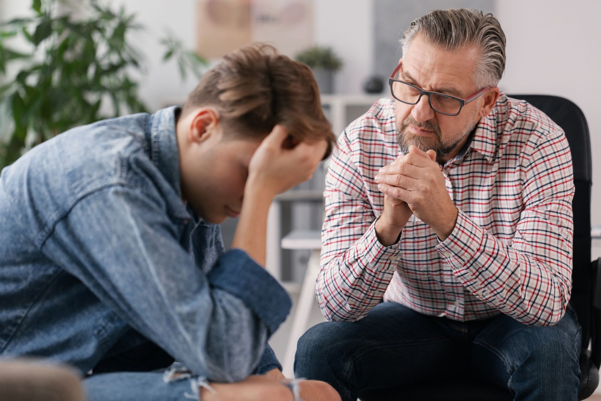 Teenager with head in hand, distressed, talking to a concerned older man in an office setting.