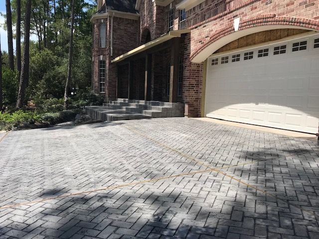 Brick driveway leading to a brick home with a garage. Gray, beige, and red tones.