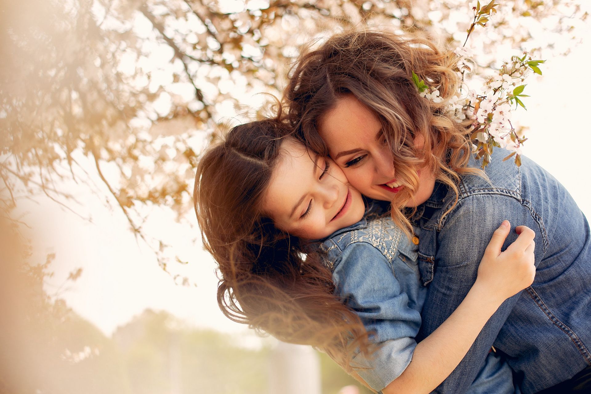Woman and child embracing under flowering tree. Sunlight bathes them in warmth.