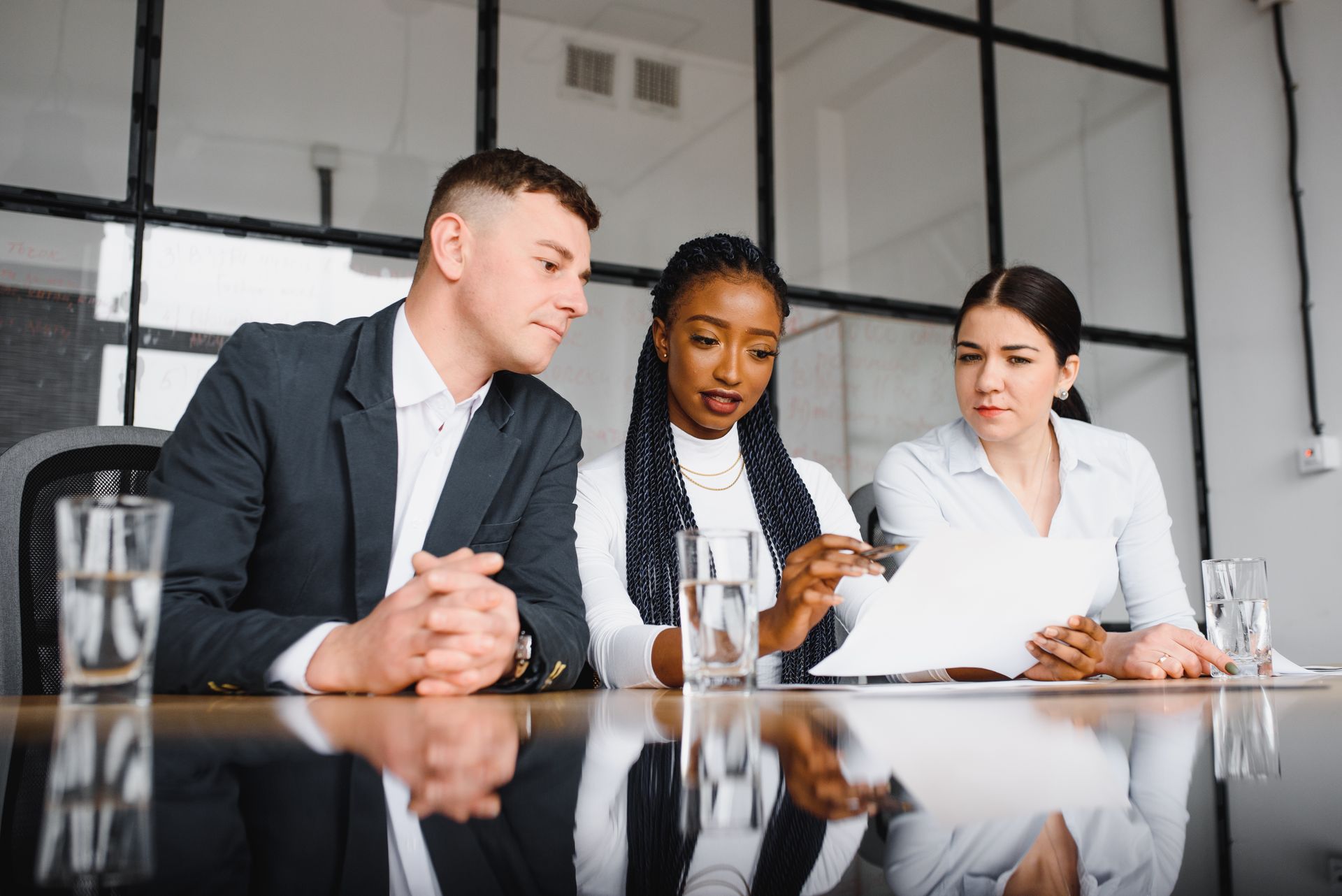 Three people reviewing documents at a table. They are in a modern office with large windows.