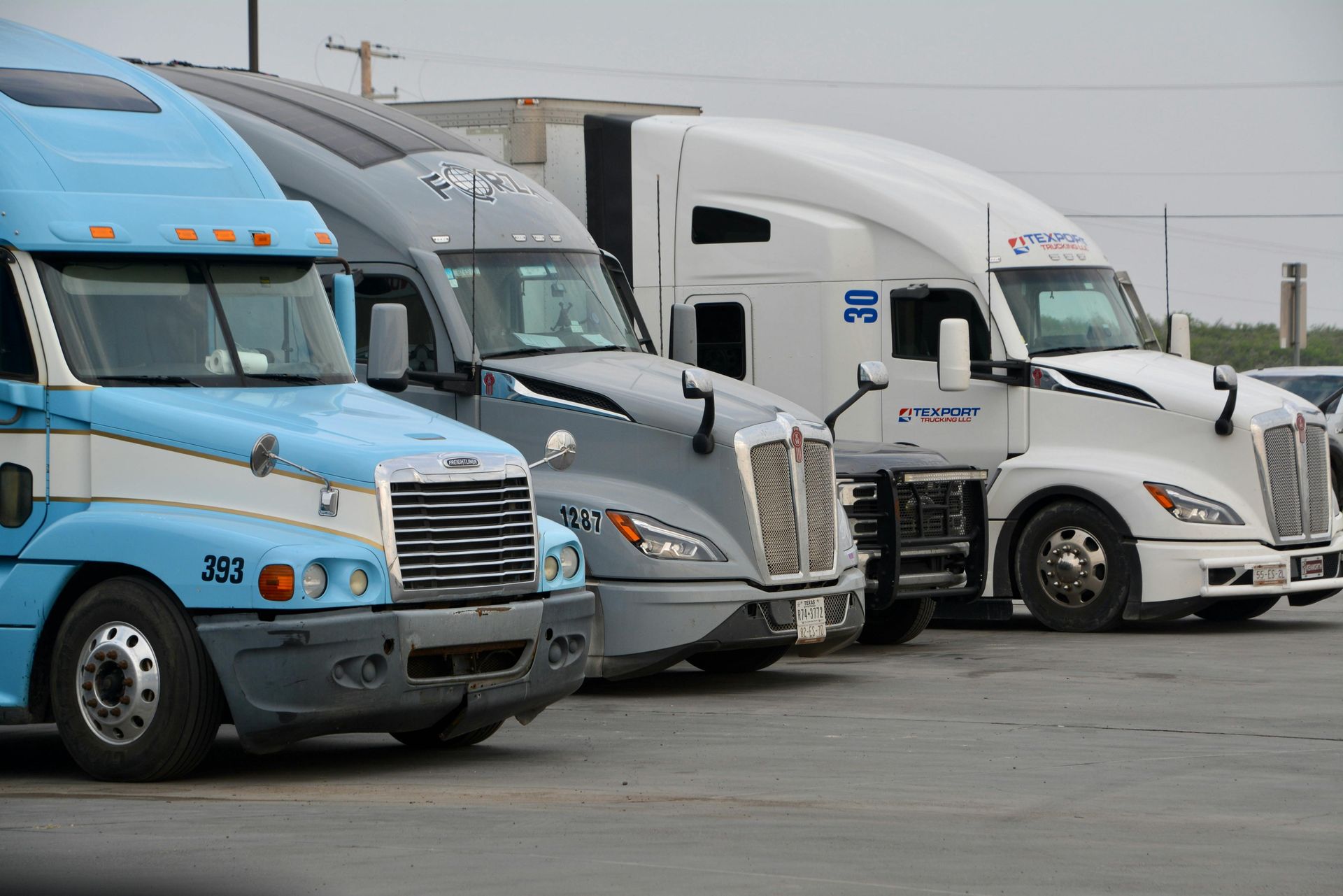 Three semi-trucks parked side-by-side: blue, gray, and white.