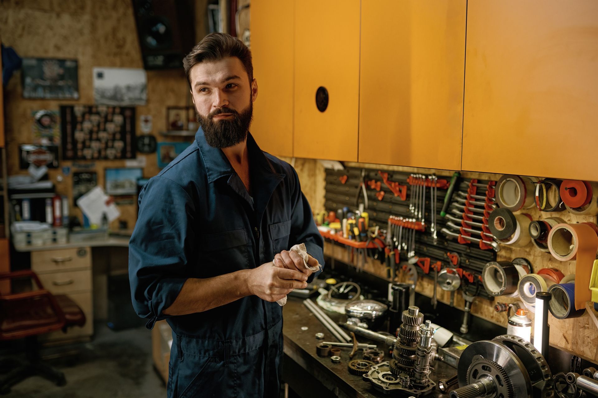 Mechanic in blue jumpsuit standing in a workshop, looking to the side, tools on wall.