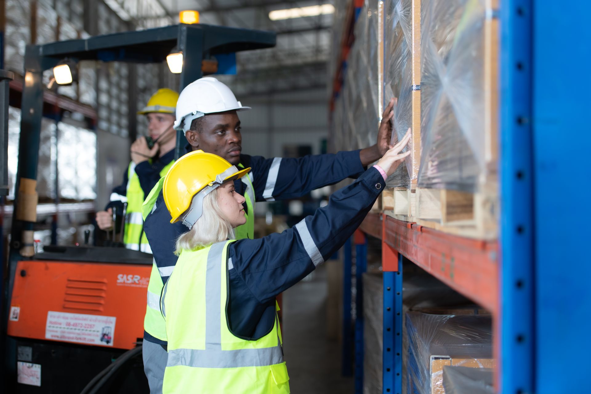 Warehouse workers inspect pallets on shelves near a forklift.