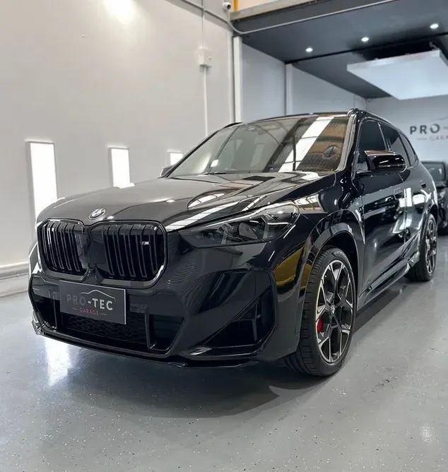 A black bmw x1 is parked in a garage for paint protection treatment