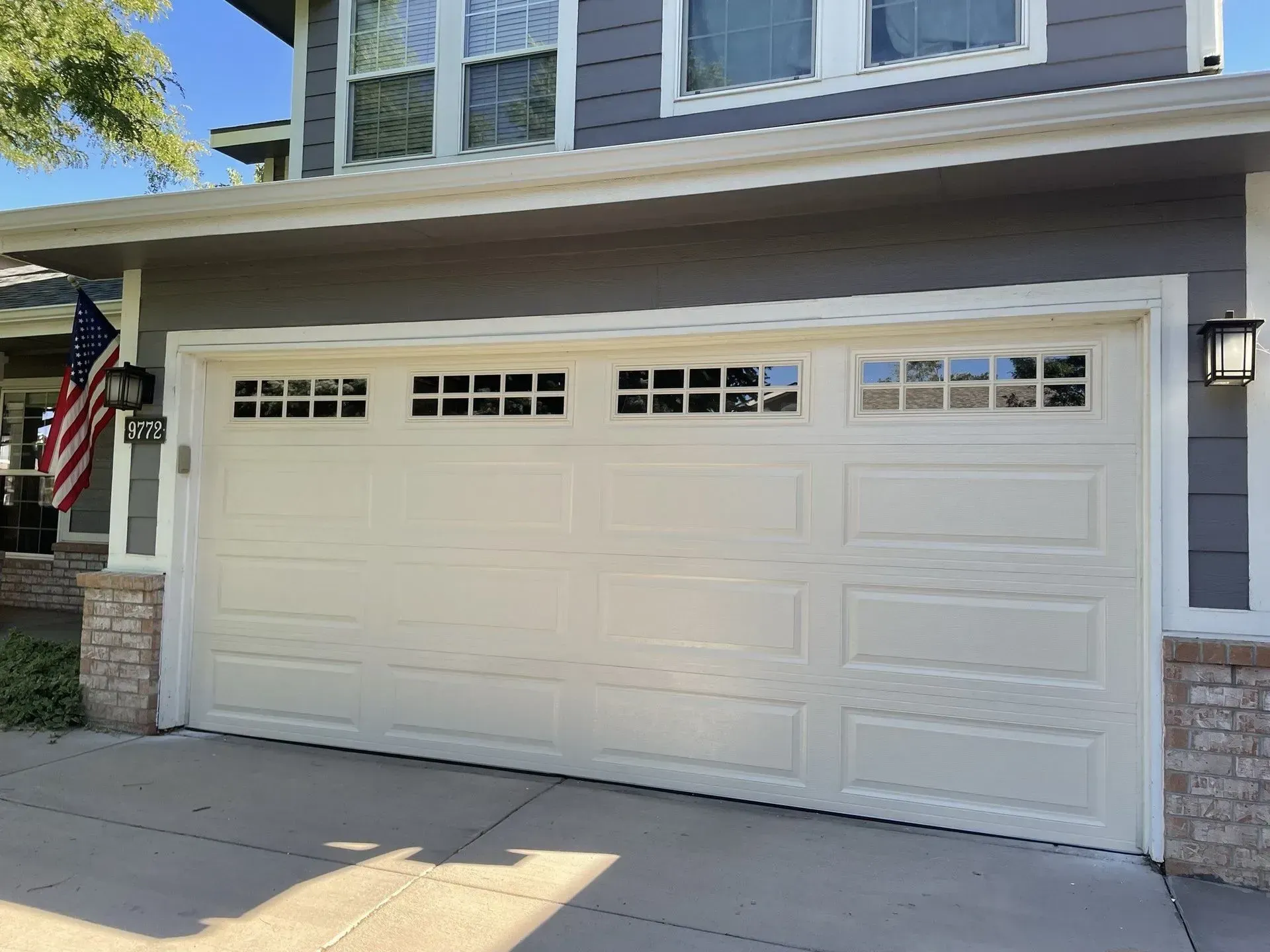 White two-car garage door on a gray house with stone trim and a small American flag.
