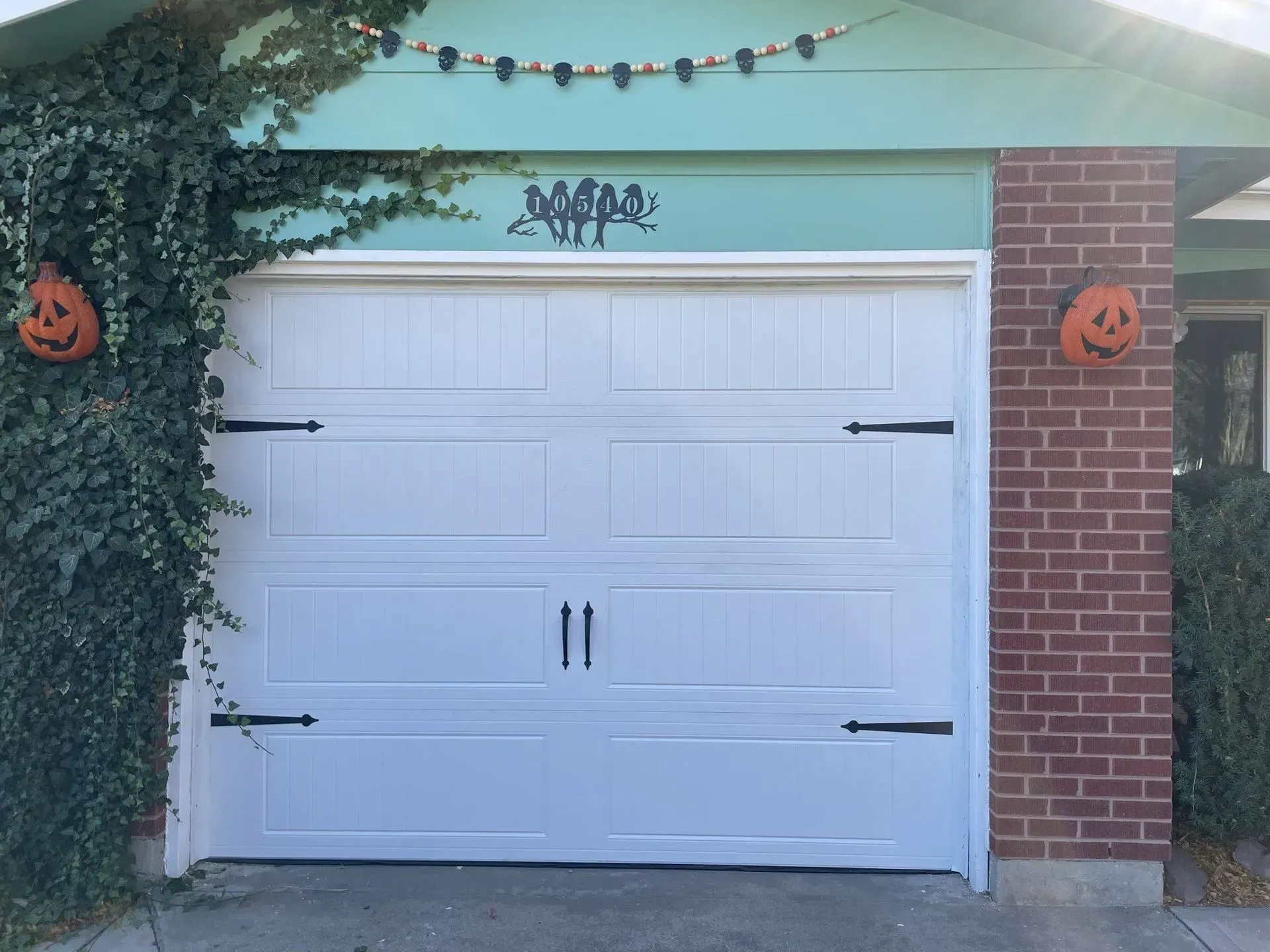 White garage door on a house with green siding, brick trim, and Halloween decorations.