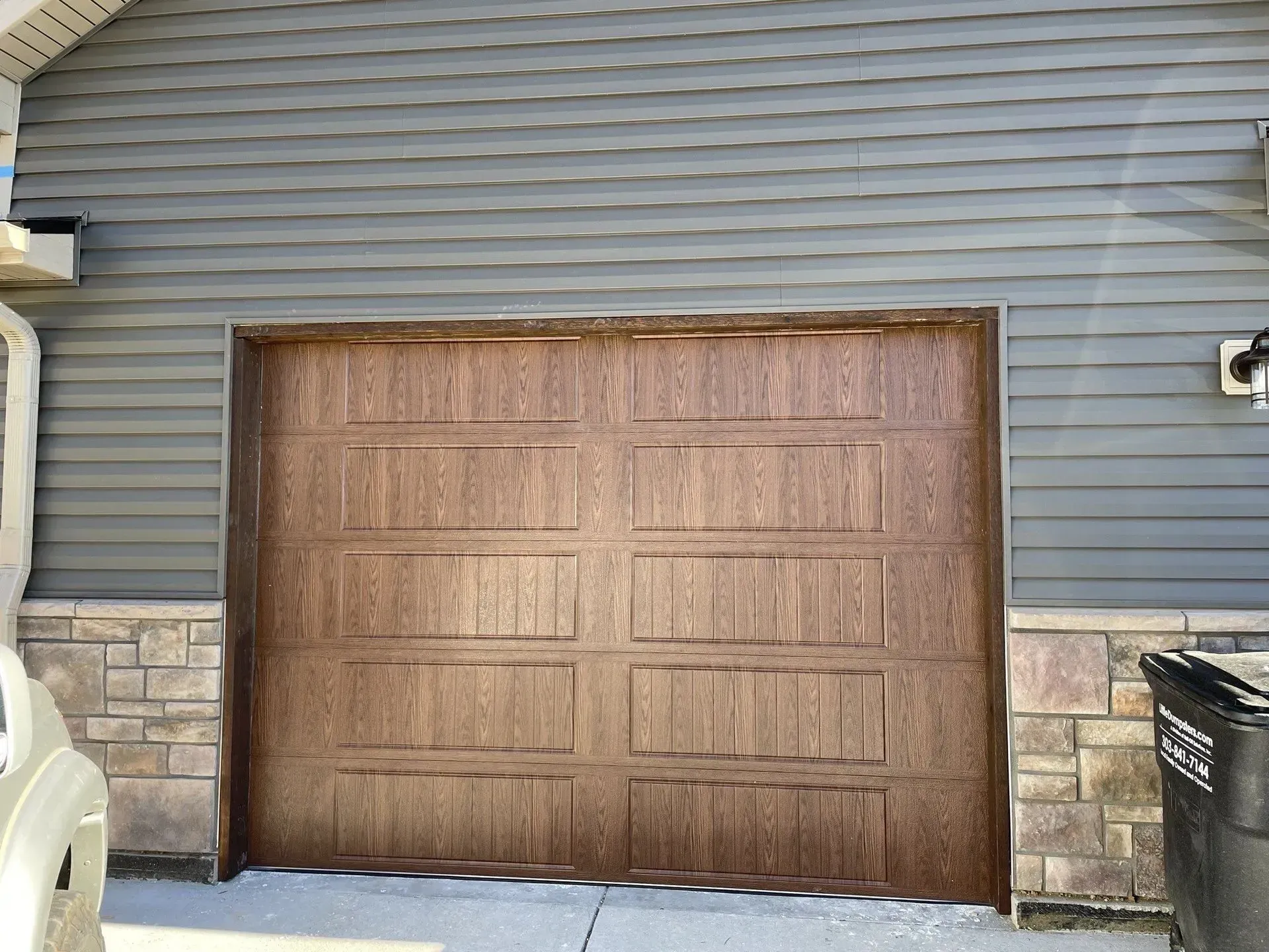 Brown garage door on a gray house exterior with stone trim and a snow-covered driveway