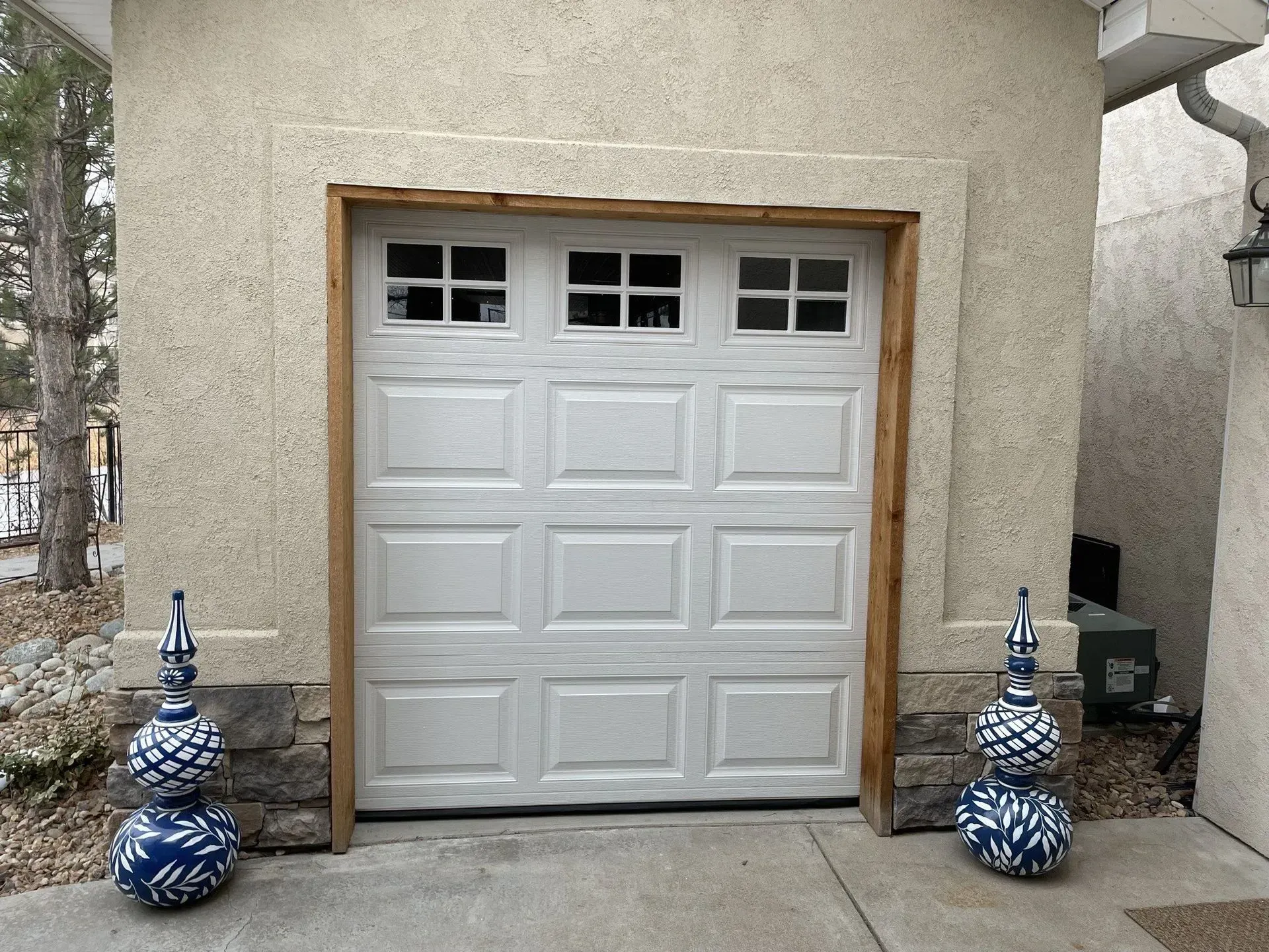White garage door centered in a stucco building, flanked by two blue-and-white decorative vases.