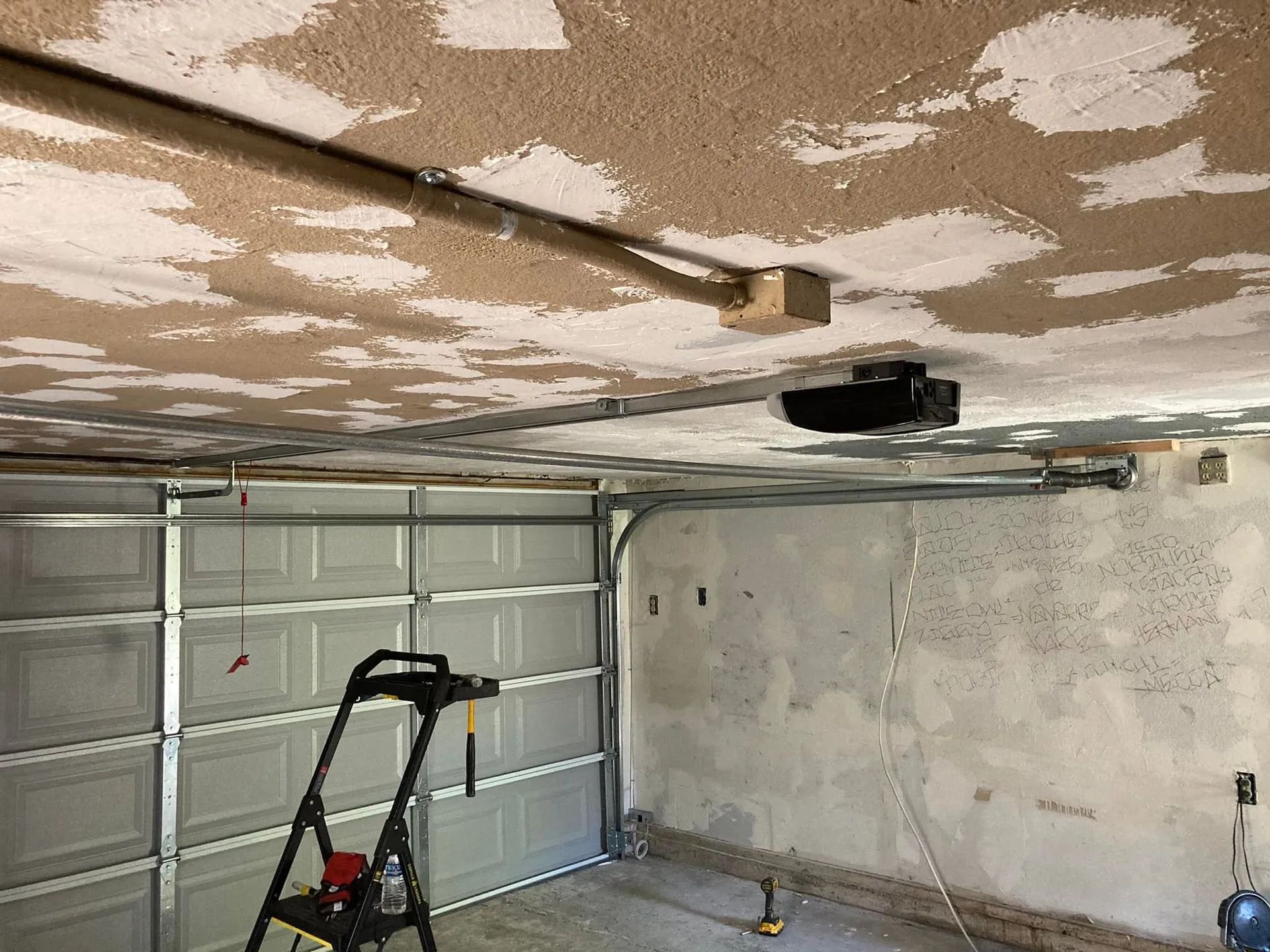 Garage interior with open door, ladder, and ceiling-mounted garage door opener on unfinished walls and ceiling