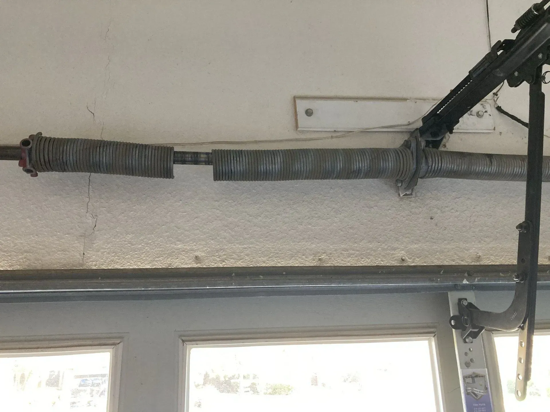 Broken garage door torsion spring wrapped around a metal shaft above two windows