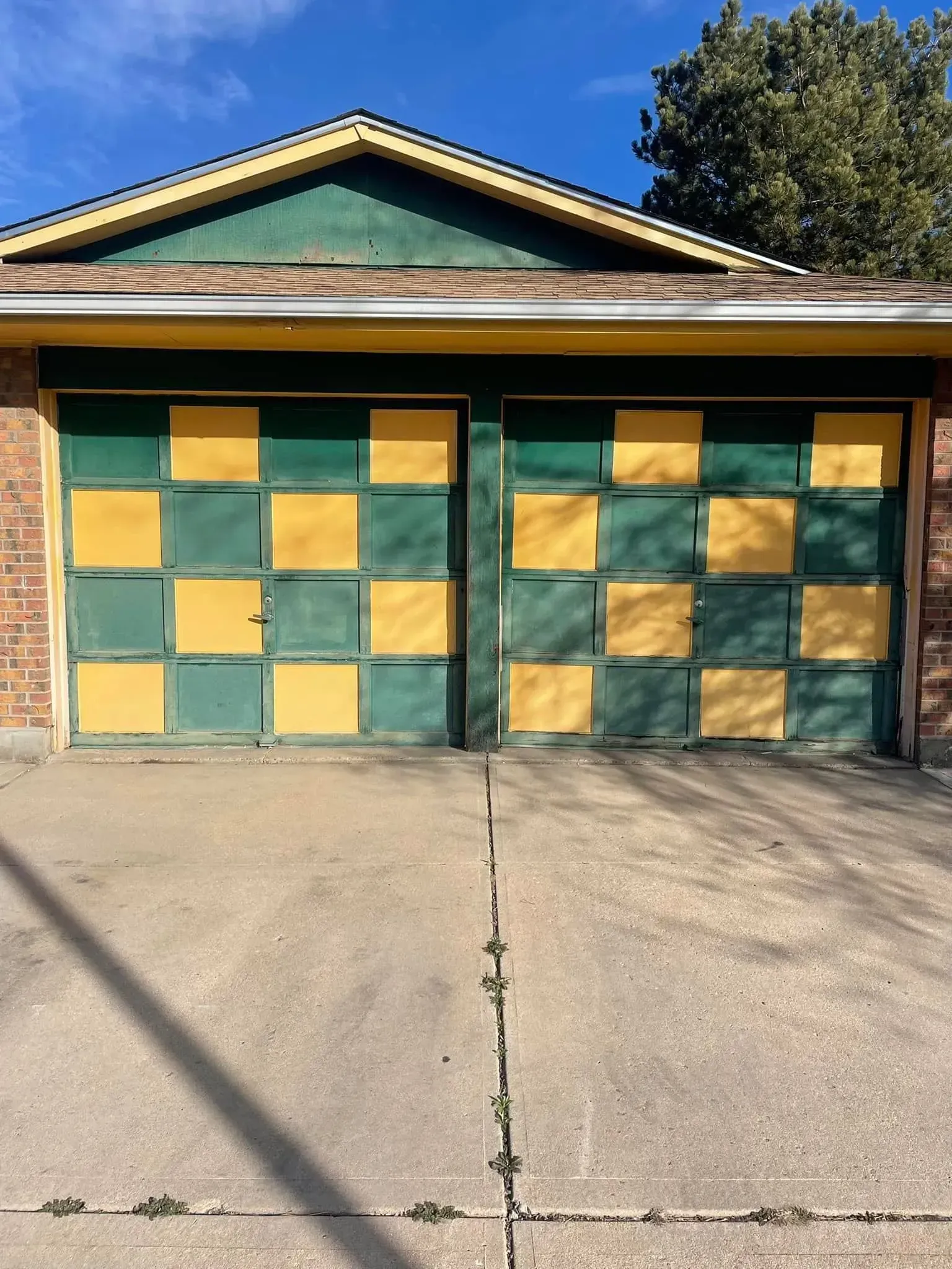 Two-car garage with green-and-yellow checkerboard doors and a concrete driveway under a peaked roof