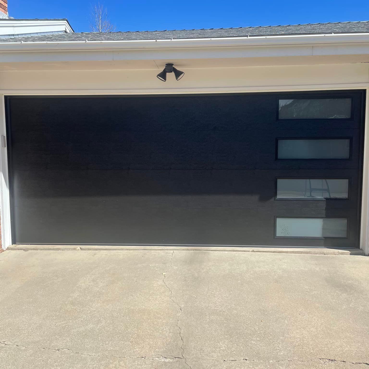 A black garage door with a lot of windows is sitting on top of a concrete driveway.