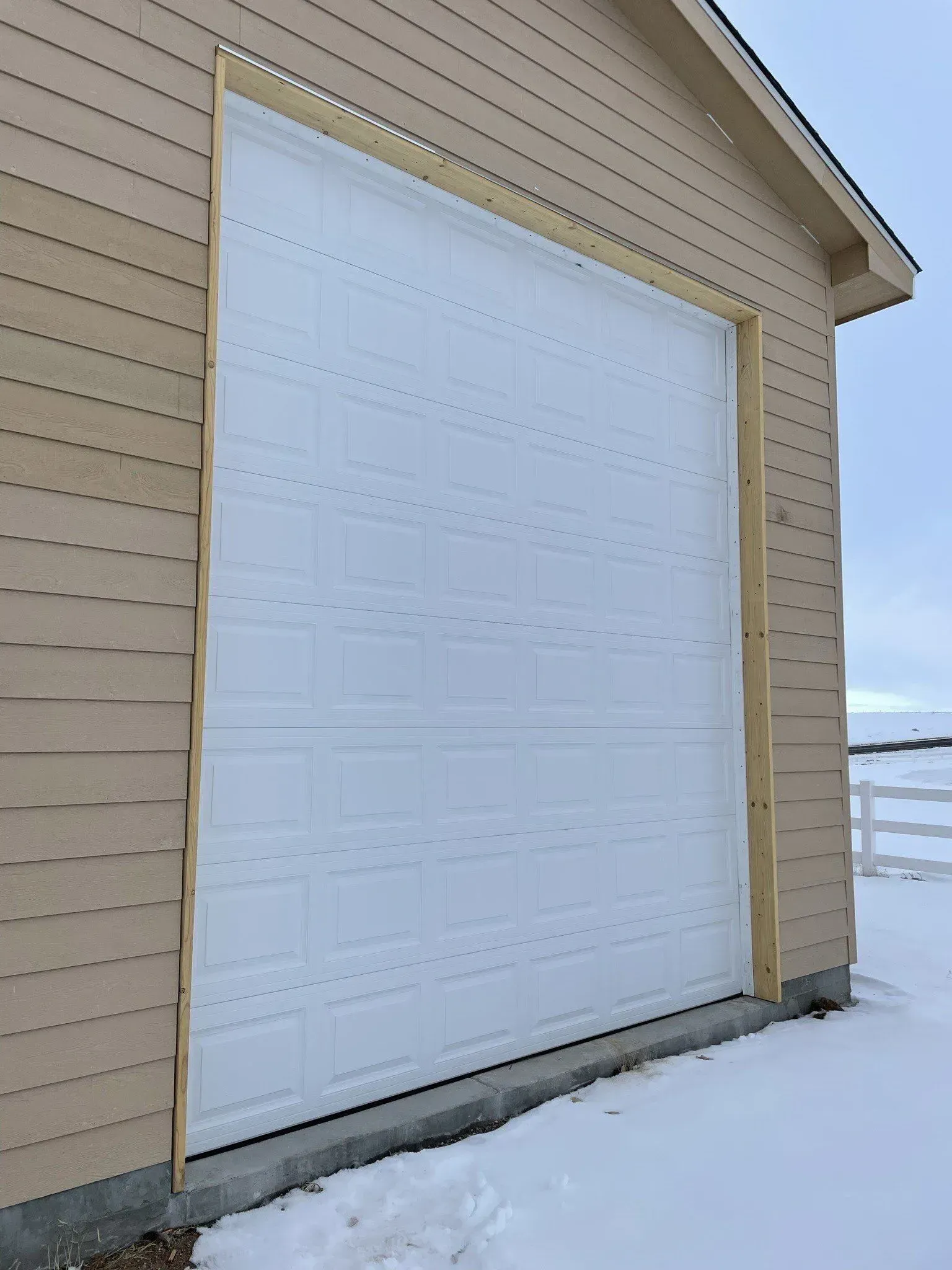 White garage door on beige siding beside snow-covered ground.