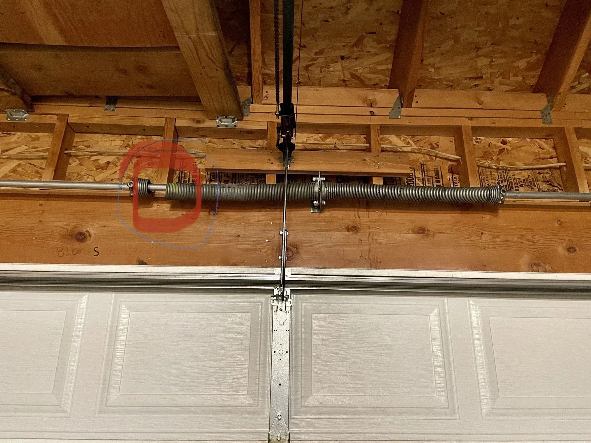 Garage door torsion spring with a red safety cable above white paneled doors.
