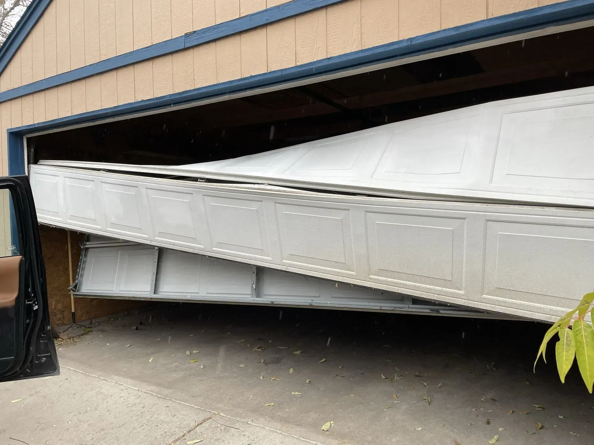 Tilted white truck trailer stuck under a low garage door opening.