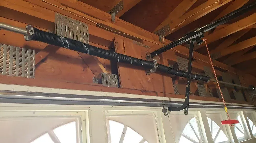 Wooden garage ceiling with a black overhead door opener rail mounted above windows.