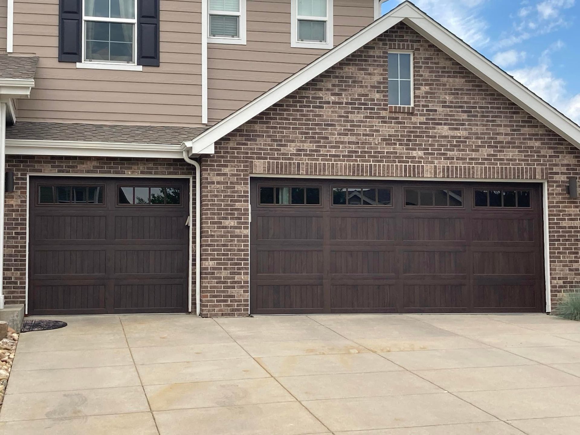 Two brown garage doors on a house with a brick facade and concrete driveway.