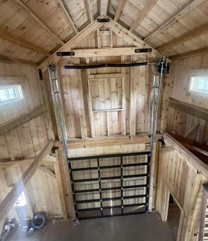 Interior of a rustic wooden barn with a large black metal loft gate and high peaked ceiling.