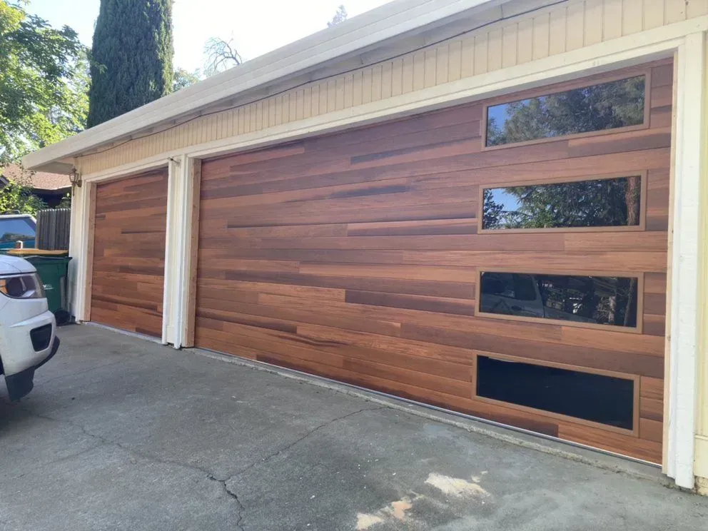 Modern wood garage door with three narrow windows beside a driveway and parked vehicle