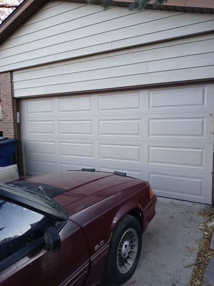 White garage door with a maroon sports car parked in front of a beige house.