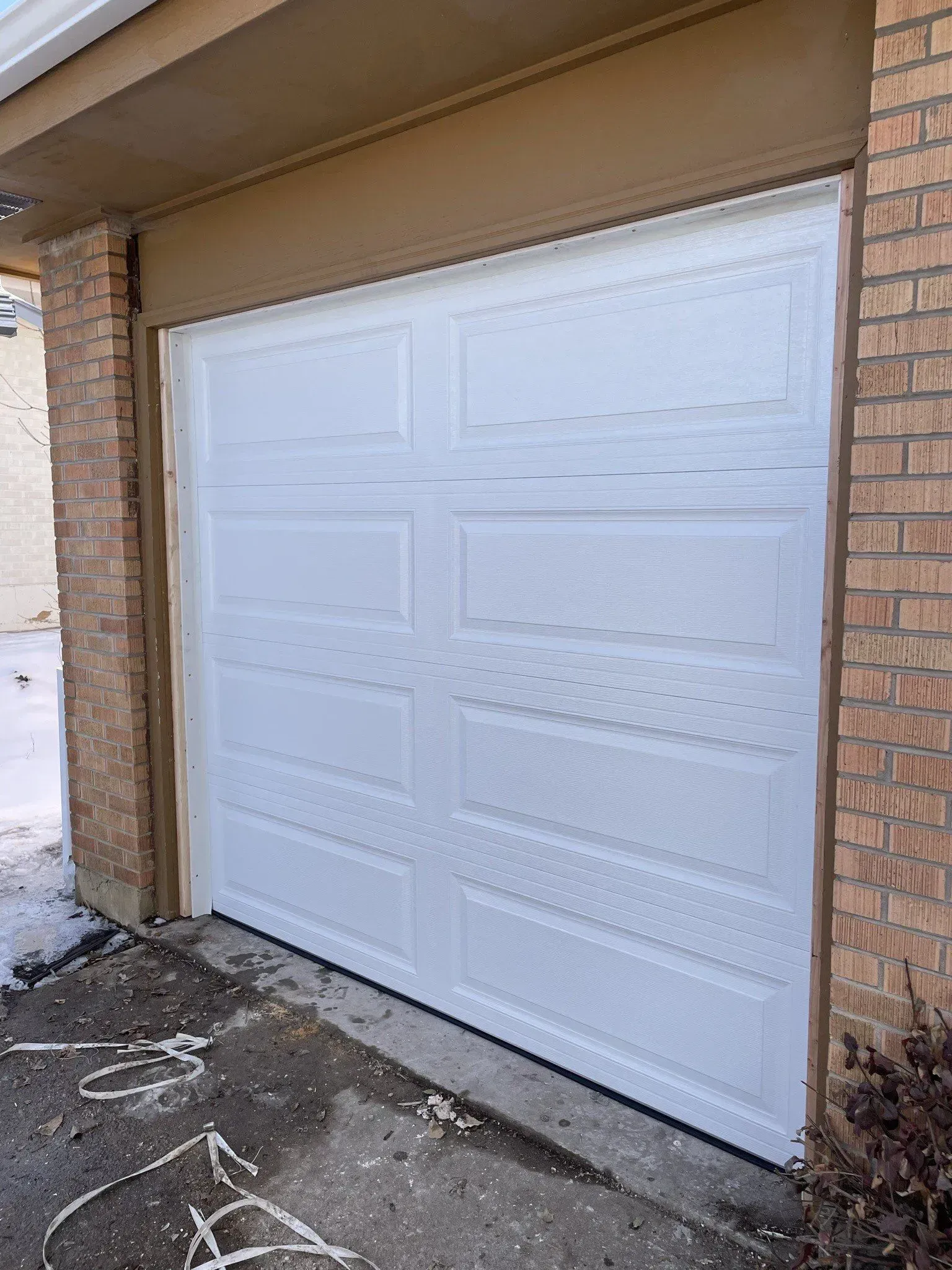 White garage door on a brick house with a concrete driveway and snow on the ground