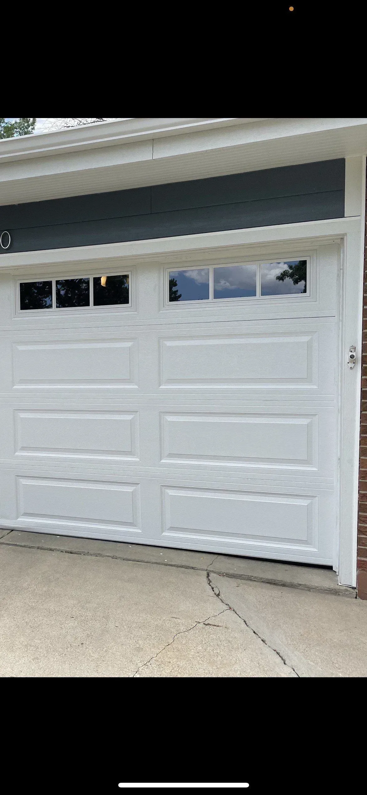 White garage door on a house with four small windows, viewed from the driveway.