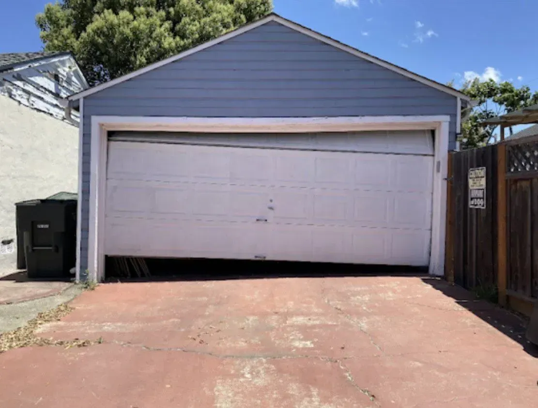 White double garage door on a house with a red driveway and blue siding, slightly ajar at the bottom
