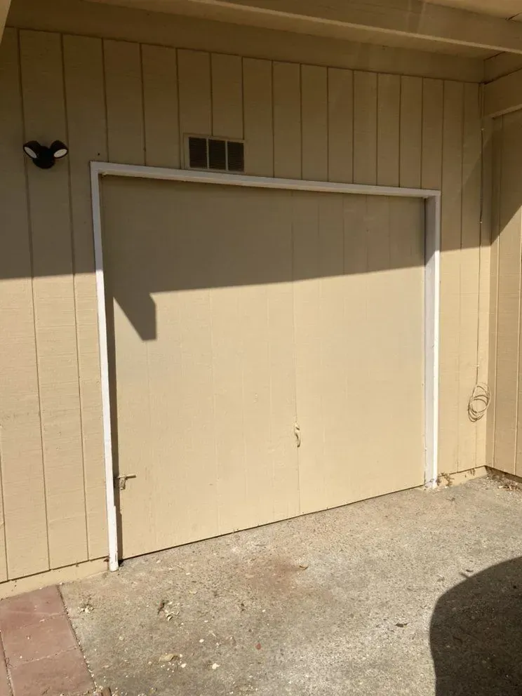 Closed beige garage door on a tan building, with a small window above and concrete driveway in front.