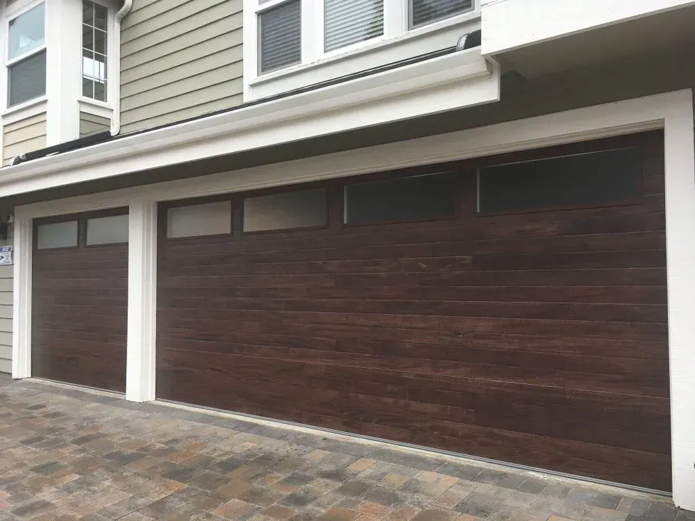 Modern two-car garage with dark wood doors and white trim on a paved driveway