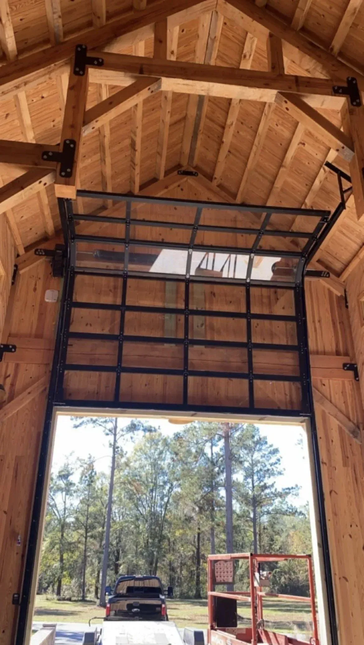 Inside wooden barn with open garage door, showing a truck and red equipment outside.