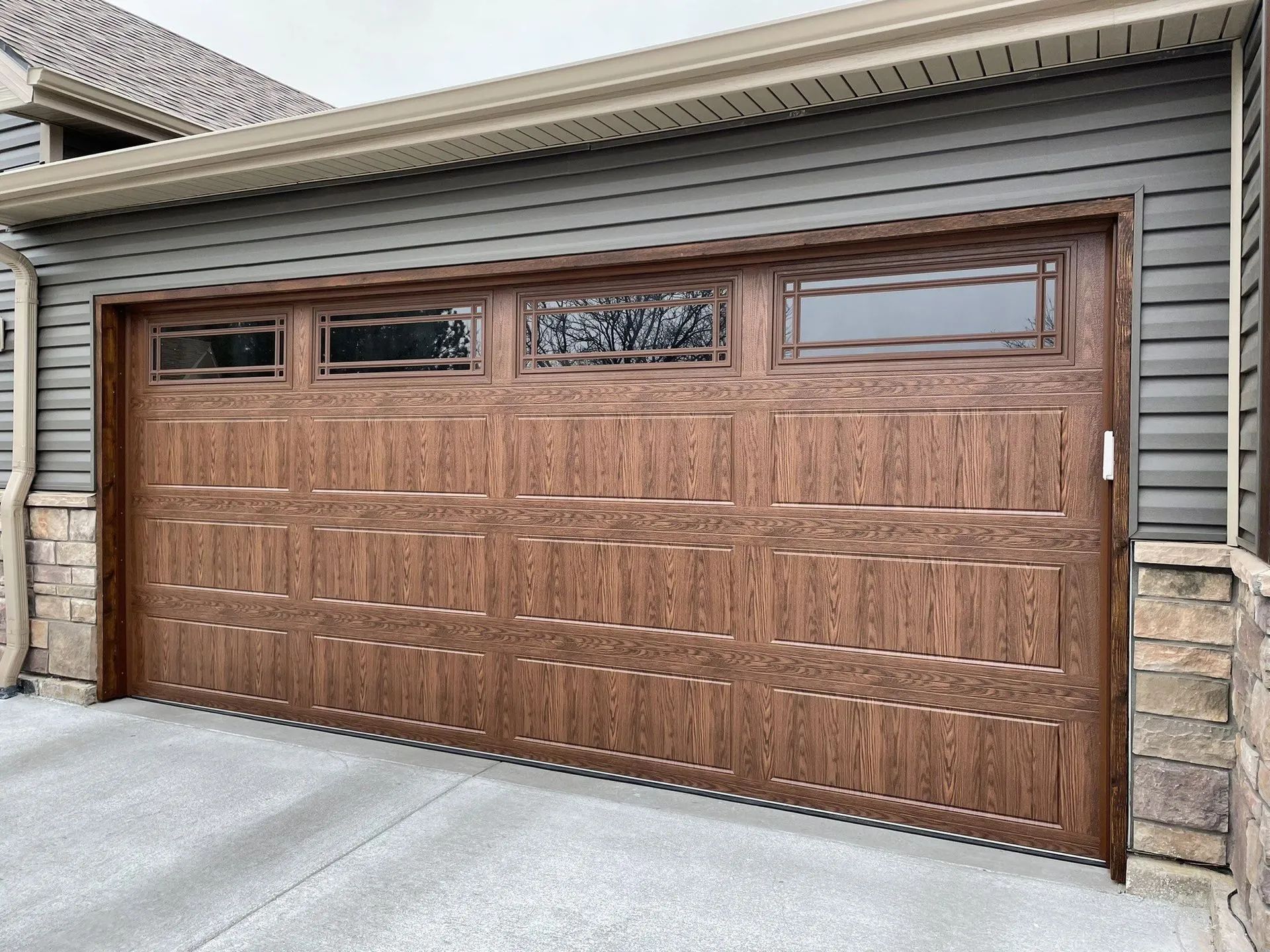 Brown wooden garage door with four small windows, set in a beige siding house exterior