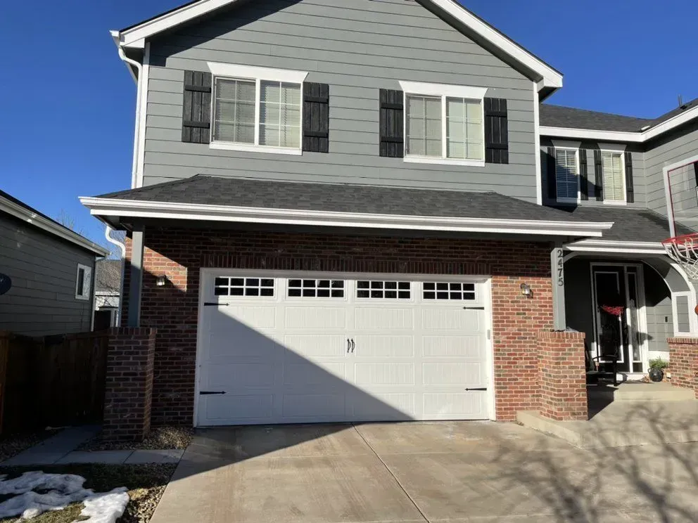 Two-story gray and brick suburban house with a white garage door and driveway in front.