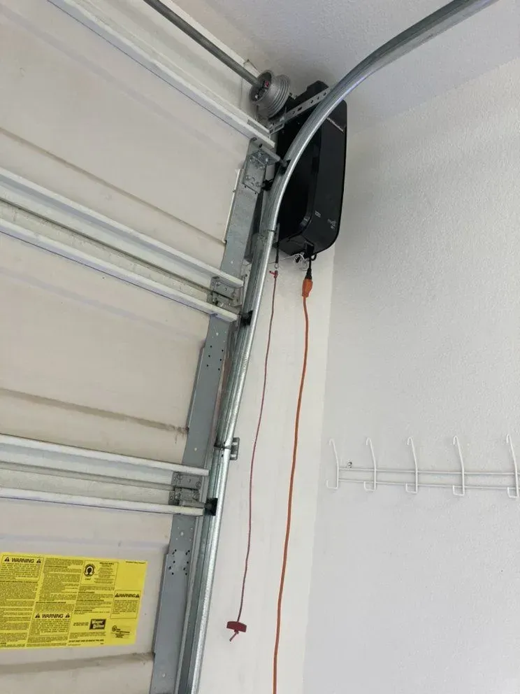 Garage door opener mounted on a curved garage ceiling, with a red emergency release cord hanging down.